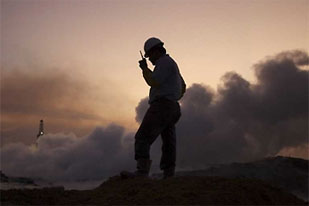A worker talking on a radio in front of smoke rising from the mud gushing out of a Lapindo Brantas Inc. gas exploration well in Sidoarjo East Java Indonesia