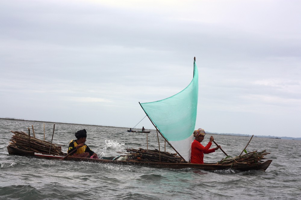 A firewood collecting team returning home in a traditional Bajau sampan. Duties are split. One steers while the other bails the boat.
