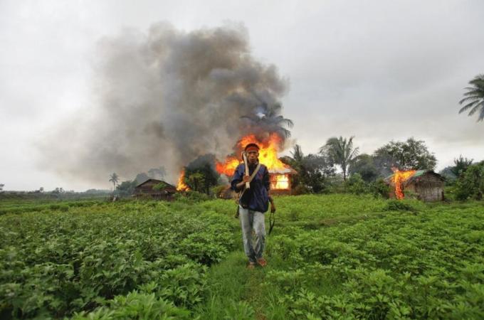 File photo of an ethnic Rakhine man holding homemade weapons as he walks in front of houses that were burnt during fighting between Buddhist Rakhine and Muslim Rohingya communities in Sittwe