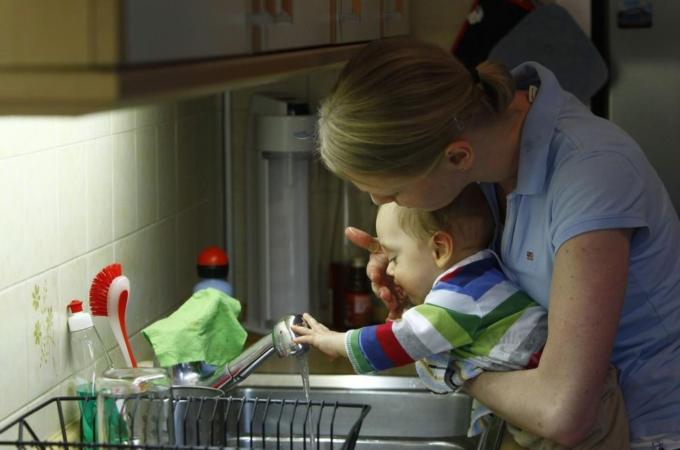 Leonard (ten-month-old) gets his mouth cleaned by mother Veronika Rixom in kitchen in Ismaning