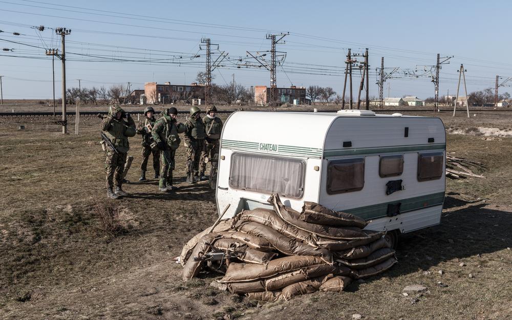 <p>Just behind the frontlines, soldiers gather around what appears to be a fortified caravan, having just been digging trenches nearby.</p>