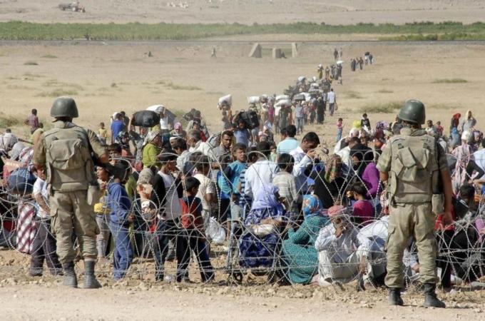 Turkish soldiers stand guard as Syrian Kurds wait behind the border fence to cross into Turkey [Reuters]
