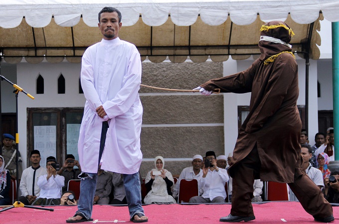 An Islamic law official whips a man convicted of gambling with a rattan cane inside a mosque compound [AP]