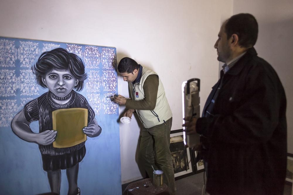 Mohammed Abusal paints at Eltiqah gallery, while fellow artist, Suhail Salem, holds a portable light. Eltiqah gallery was founded in 2001.