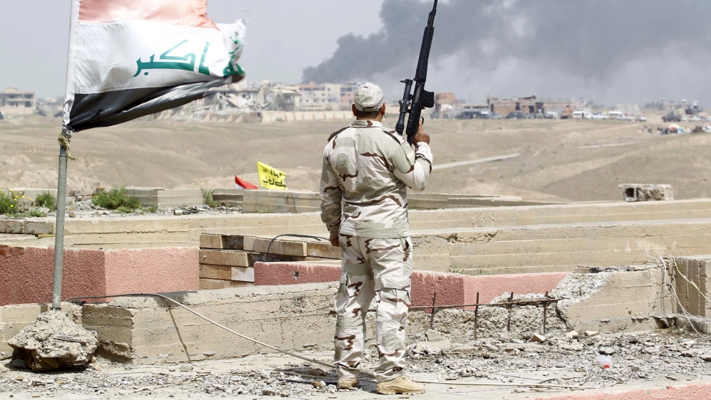 A member of the Iraqi security forces carries his weapon as he watches smoke rise from a scene of clashes between the Iraqi army and Islamic State militants in Tikrit