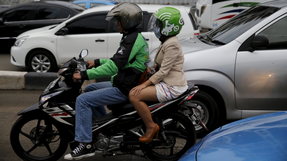 A Gojek driver carries a passenger through a business district in Jakarta. Gojek’s app lets users book motorcycle taxis to navigate the city’s gridlock