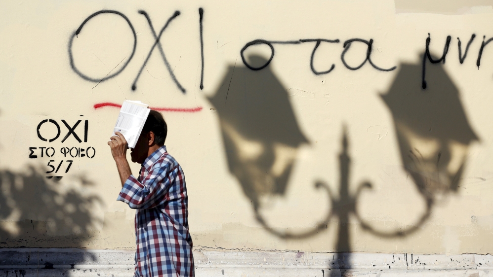 A man shelters from the sun as he walks past graffiti that reads "No" in Greek in Athens [REUTERS]