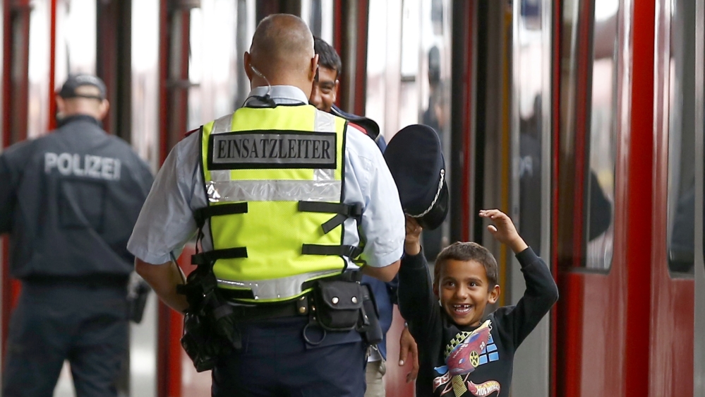 Migrant boy tries on Bahn security officer''s cap after arriving by train from Salzberg at station in Munich