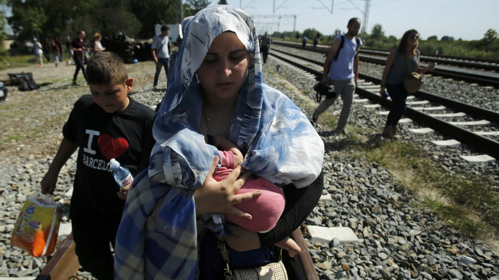 A migrant woman carries a baby as she walks on a railway track near Tovarnik