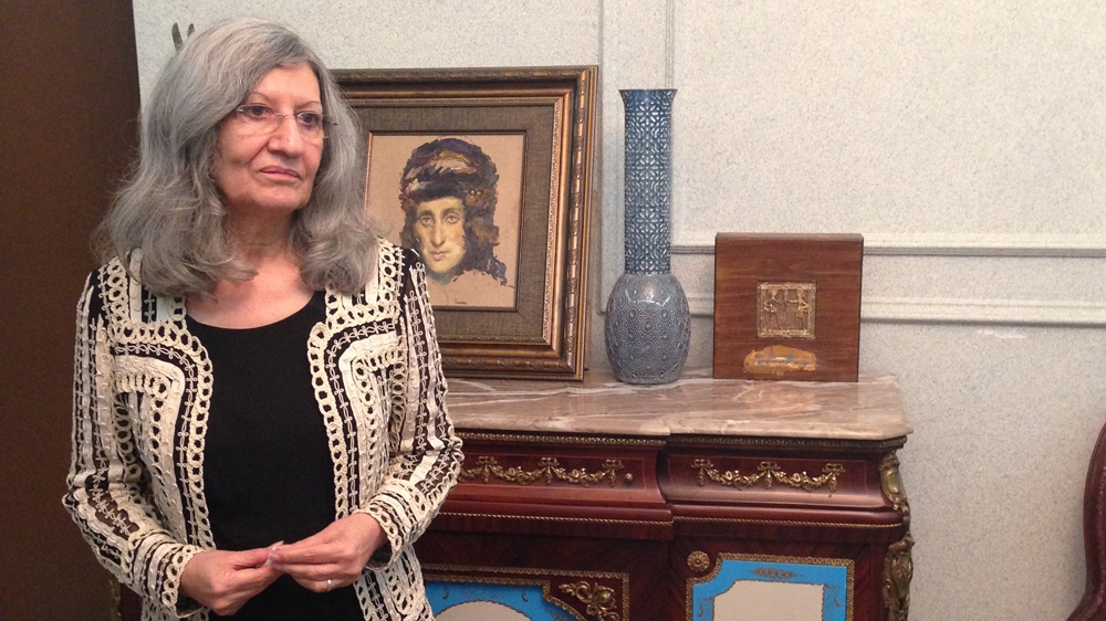 Hero stands in front of a painting of the iconic Kurdish feminist Hapsa Khan in her home in Sulaimania [Lara Fatah/Al Jazeera]