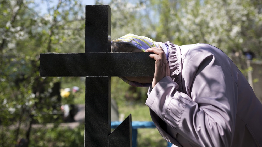 The mother of Andrey Papov, who died in a mining accident at the age of 34, kisses his grave on the first Sunday after Easter, when Russian Orthodox families visit their dead relatives. [Janos Chiala and Tali Mayer/Al Jazeera] 
