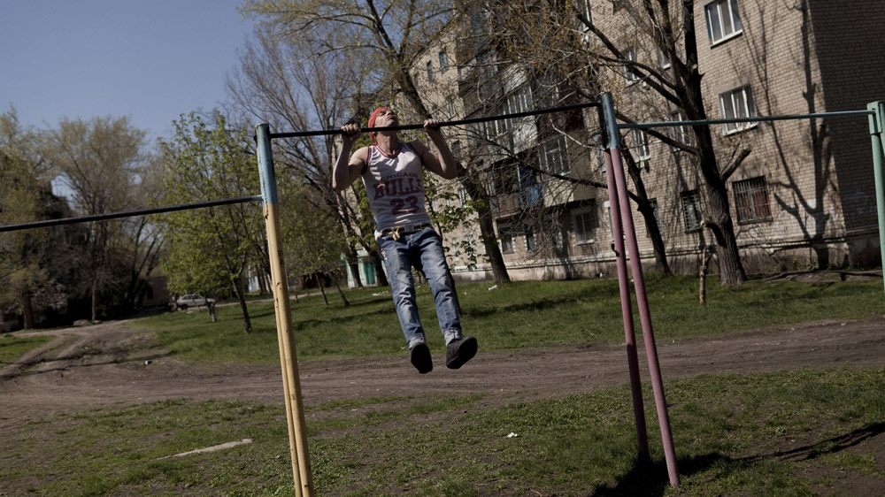 Twenty-seven-year-old Andrej plays a game of lientochka in Krasnodon. This is when two people challenge each other to do a certain number of pull-ups, adding one more at each turn. His opponent gave up when they reached 11 so Andrej continued on his own. [Janos Chiala and Tali Mayer/Al Jazeera] 