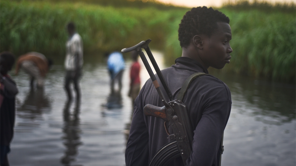 A man with a gun stands watch over displaced people, who have taken shelter from fighting, in a rebel-held part of Leer county, in Unity State, South Sudan [Jason Patinkin/AP]