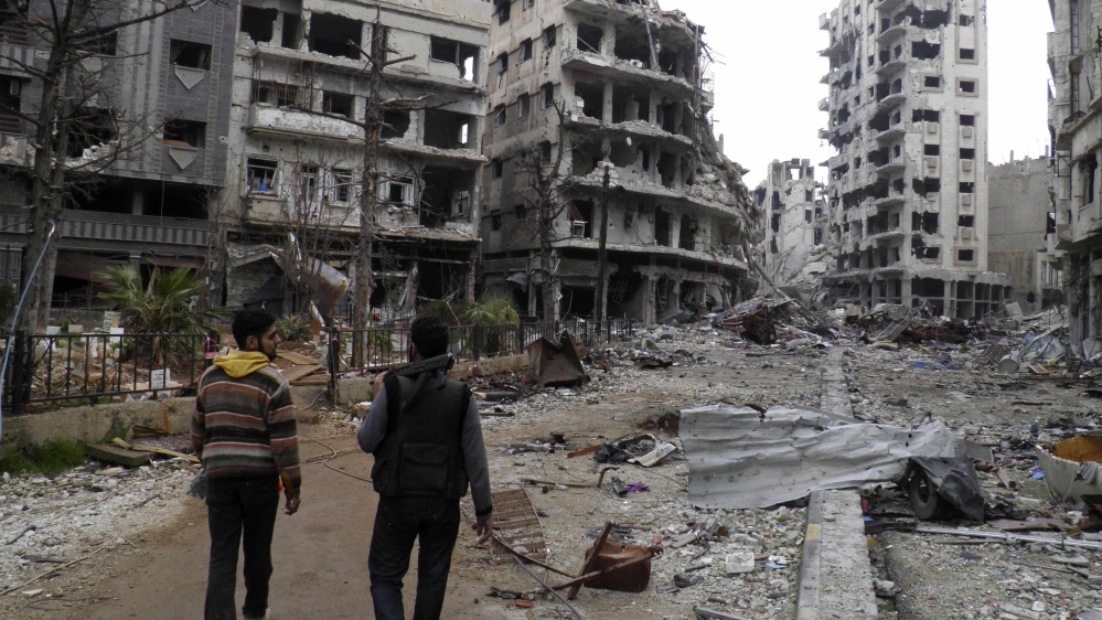 Free Syrian Army fighters walk along a deserted street past damaged buildings in the besieged area of Homs