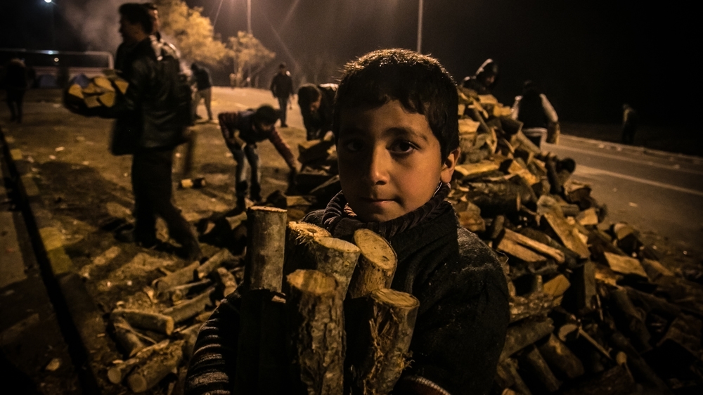 A child collects wood for the night at the petrol station of Polikastro, 20km from the Idomeni border, where thousands of people are stranded [Nicola Zolin/Al Jazeera] 