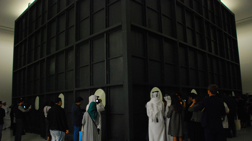 Visitors watch the fire hose pumping with water inside a tank entitled 'Freedom' at Al Riwaq gallery [Anna Nigmatulina/Al Jazeera]