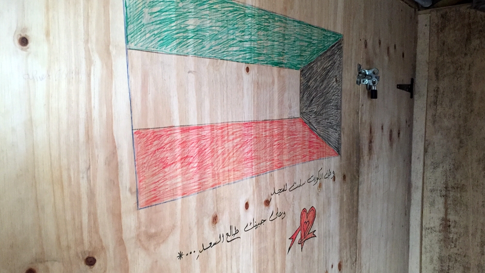 A Kuwaiti flag and verses from the national anthem at the entrance of one shack [Shafik Mandhai/Al Jazeera]