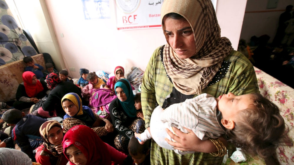 A displaced woman carries her child in a building that is used as a temporary shelter in Makhmour
