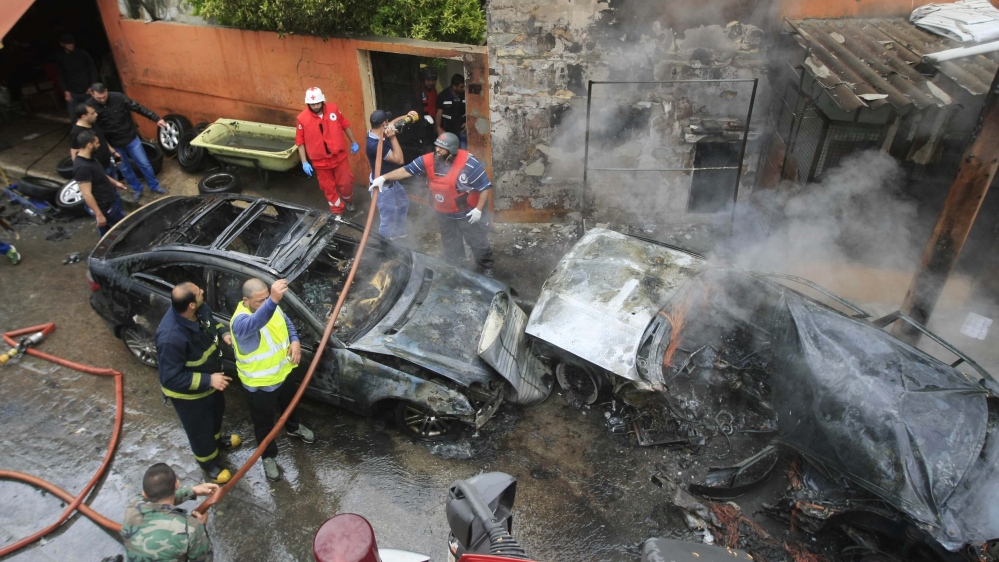 Civil defense workers and firefighters gather next to burned cars