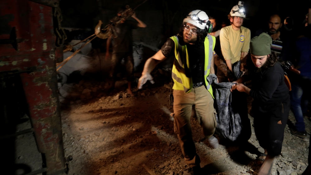A rebel fighter and civil defence members carry a body removed from under debris after the strike [Reuters]
