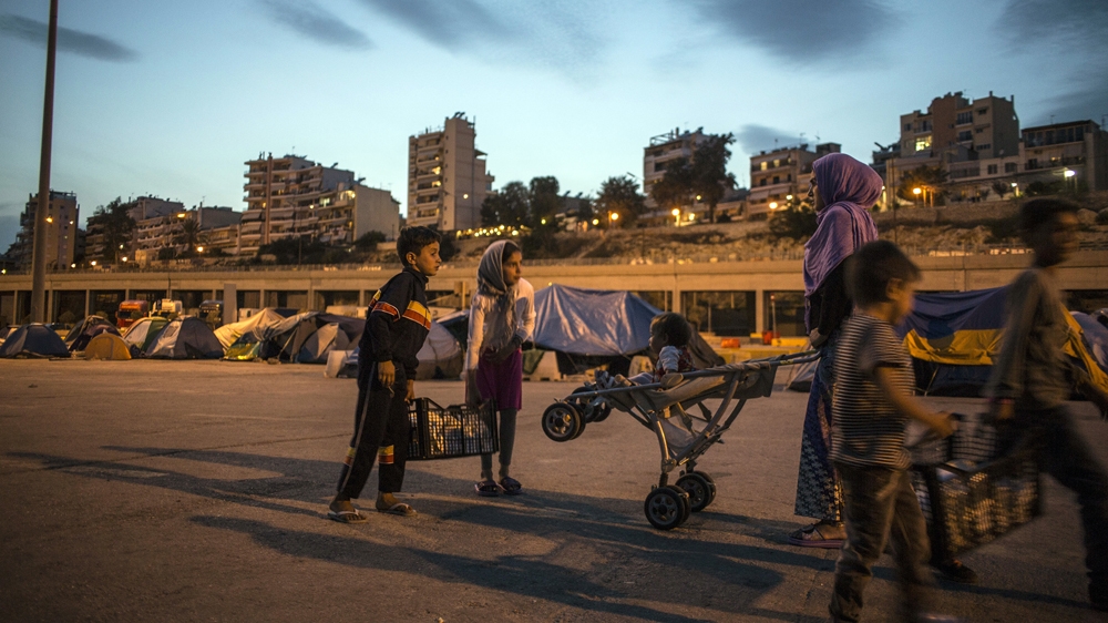 A family of Syrians collect supplies at dusk against a background of the multi-storey apartment buildings that compose most of central and suburban Athens [Iason Athanasiadis]