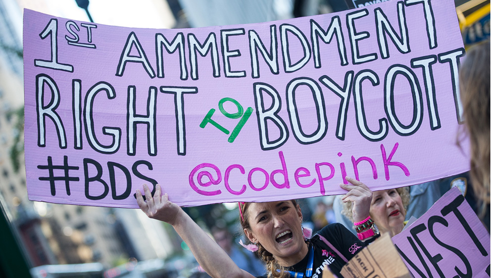 A woman holds up a sign at a protest on June 9, 2016 against the New York governor for issuing an anti-BDS executive order [Sainatee Suarez/Al Jazeera] [Al Jazeera]