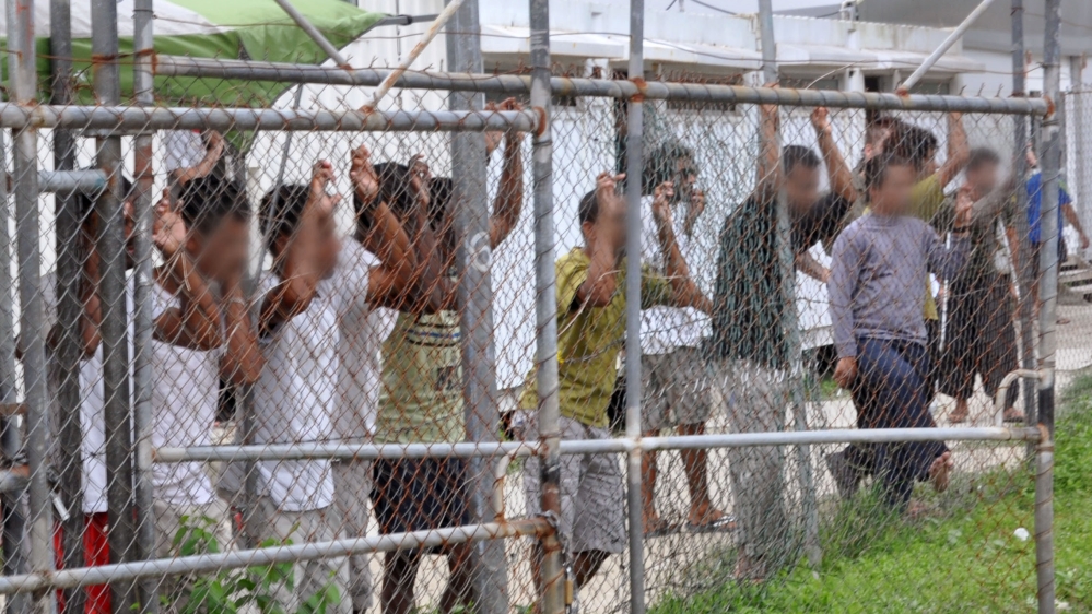 Asylum seekers look at the media from behind a fence at the Manus Island detention centre, Papua New Guinea