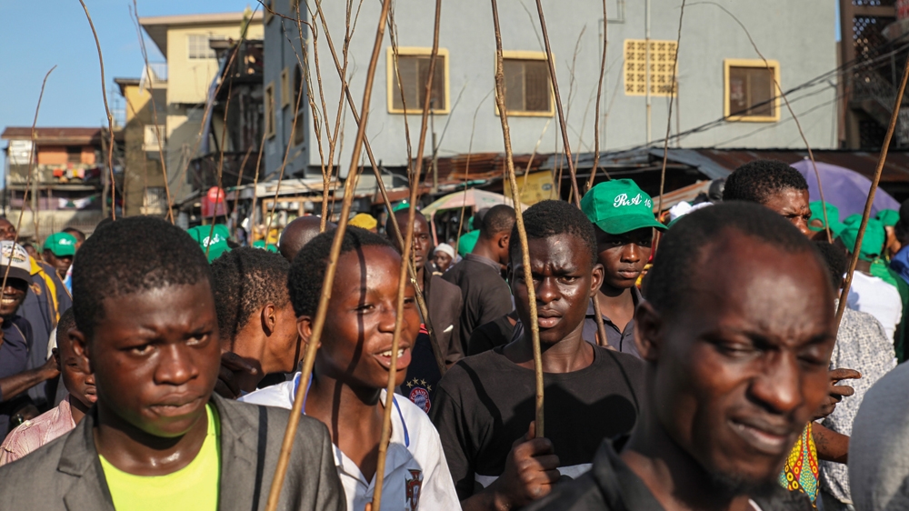Young men carry tree branches as they pursue the Agodongbo masquerade through the Brazilian quarter of Lagos, Nigeria [Chris Stein/Al Jazeera] 
