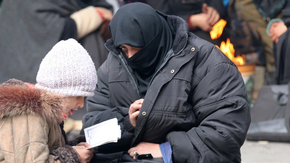 A woman sits with her child reading the Koran while waiting to be evacuated with others from a rebel-held sector of eastern Aleppo