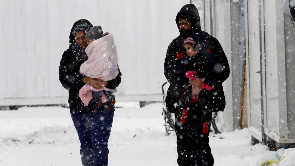 Stranded Syrian refugees carry their children through a snow storm at a refugee camp north of Athens
