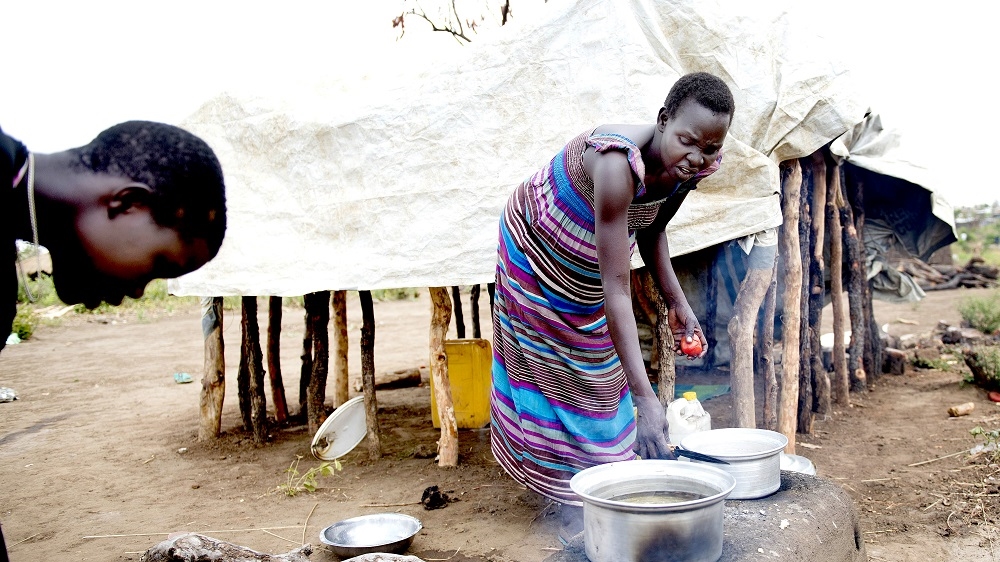 Rose Tamaka cooks outside her clay hut in the Bidibidi settlement [Yilmaz Polat/Al Jazeera]