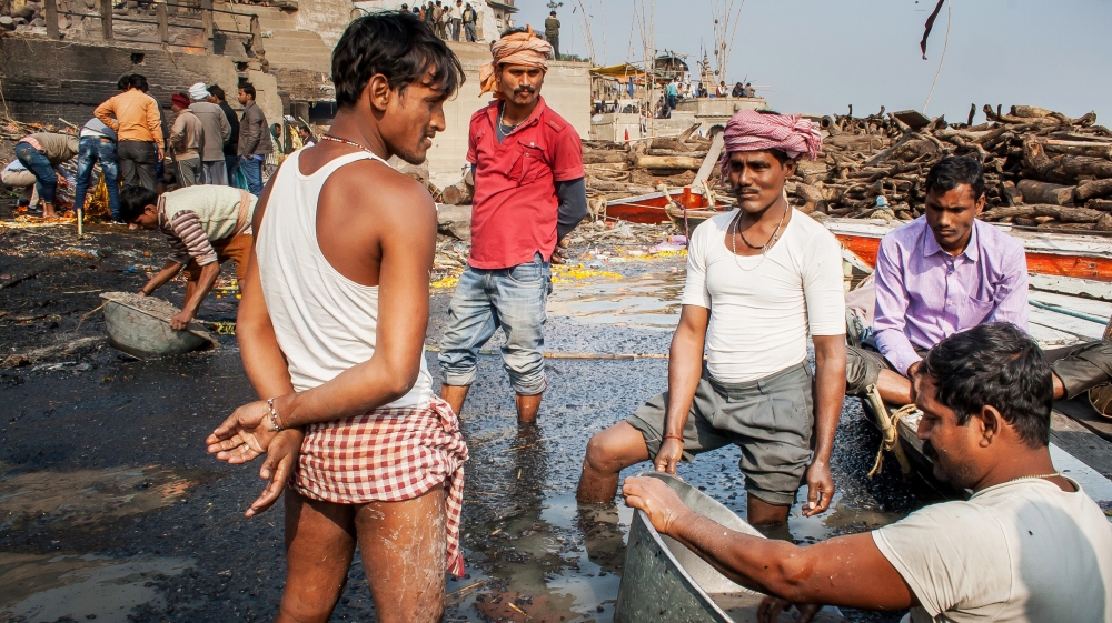 Dom men sift through ash to cull tiny pieces of melted gold and silver - remnants of jewellery that the deceased were wearing. Yogi's oldest brother performs this task to earn for his family. [Radhika Iyengar/Al Jazeera]