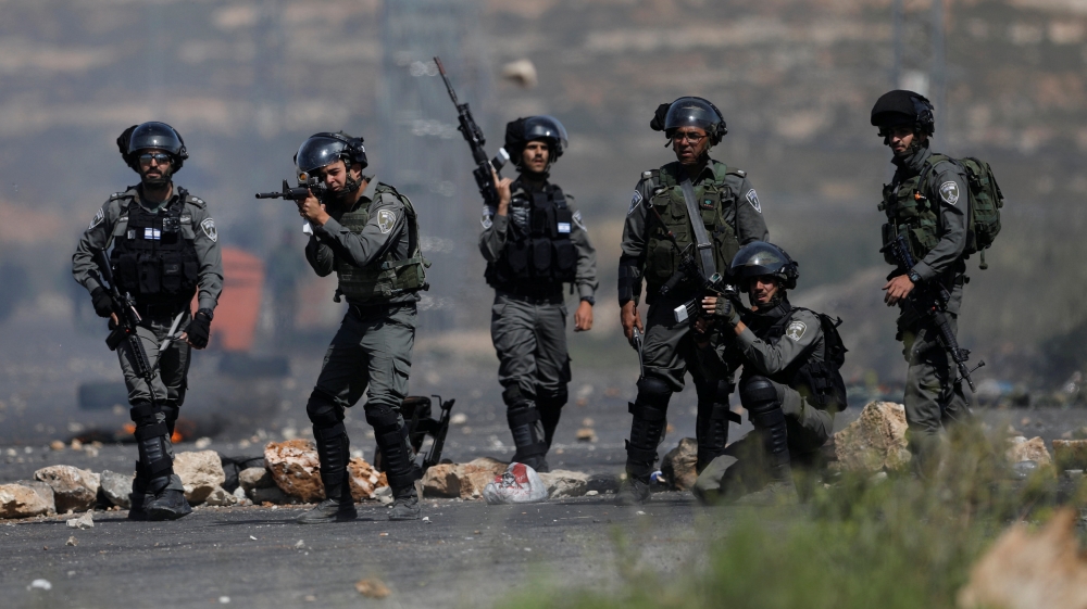 An Israeli border policeman aims his weapon at Palestinian protesters during clashes at a protest in support of Palestinian prisoners on hunger strike in Israeli jail, near Ramallah