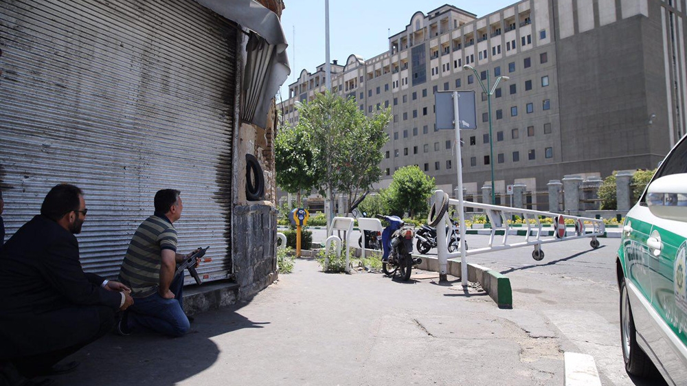 An undercover Iranian policeman, left, holds a weapon outside the Iranian parliament during an attack on the complex [Omid Vahabzadeh/Fars News via AFP]
