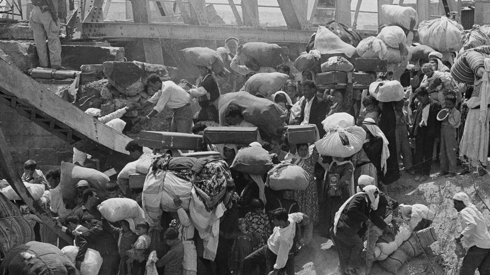 
Palestinian refugees carry their belongings as they prepare to cross the wrecked Allenby Bridge over the Jordan River from the Israeli-occupied West Bank on June 22, 1967 [AP]
