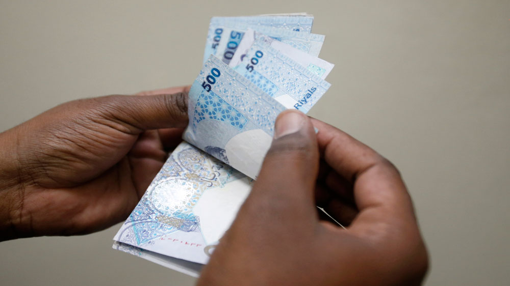 A man counts Qatari riyal notes at a money changer in Doha