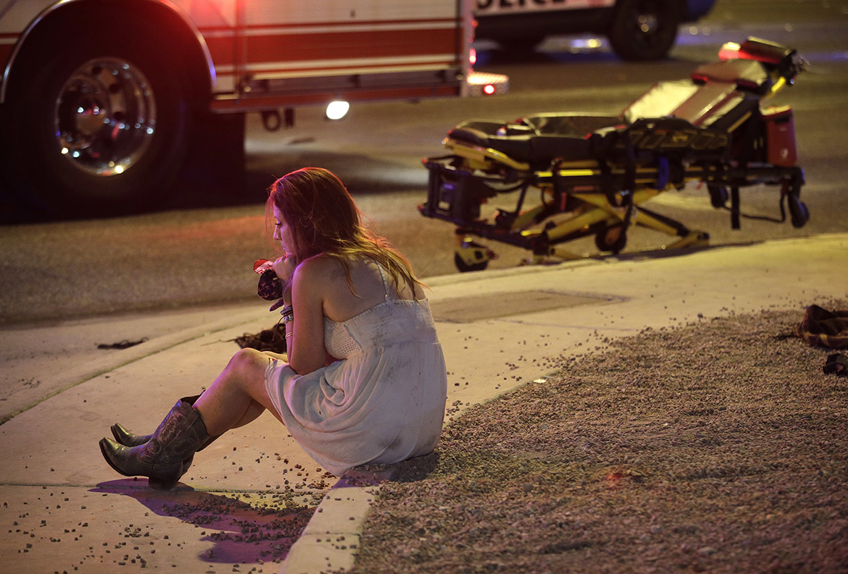 A woman sits on a curb at the scene of a shooting outside of a music festival along the Las Vegas Strip, Monday, Oct. 2, 2017, in Las Vegas. Multiple victims were being transported to hospitals after
