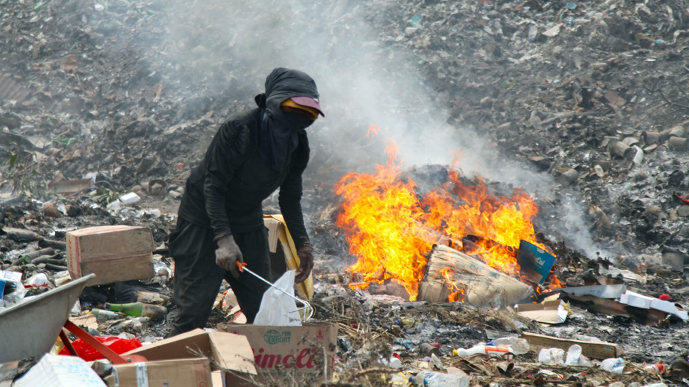Wafts of acrid black smoke rise from fires set by scavengers to melt plastic away from scrap metal [Ian Lloyd Neubauer/Al Jazeera]
