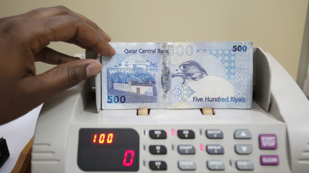A cashier counts Qatari riyal notes at a money changer in Doha