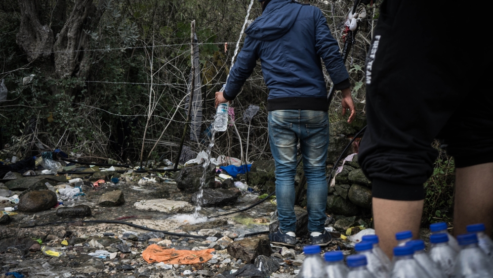 Iraqi refugees fill water bottles from a hose outside the Moria camp [Patrick Strickland/Al Jazeera]