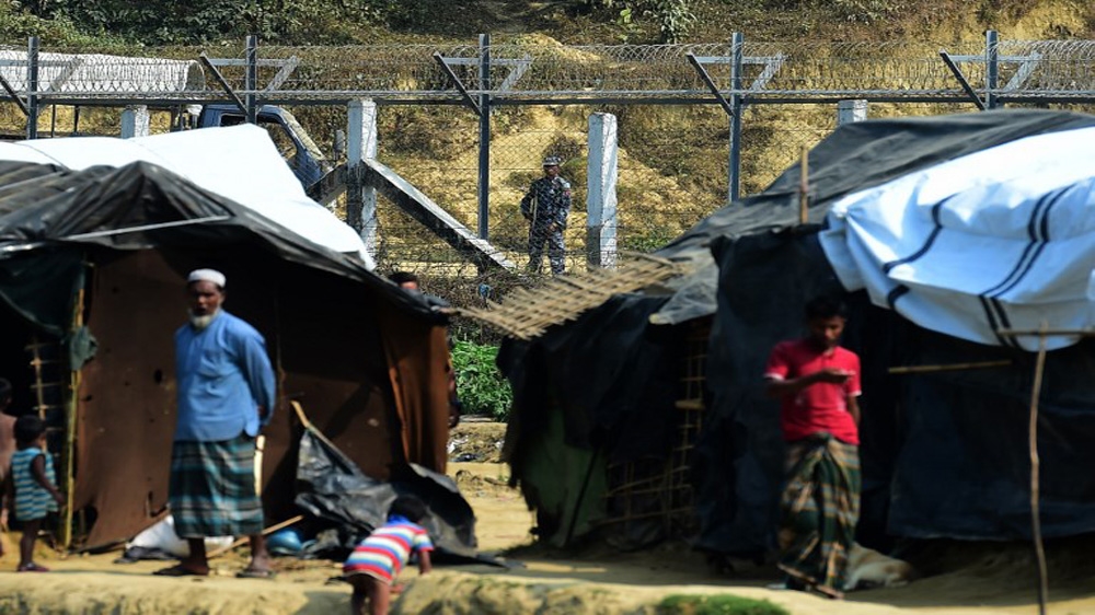 A Myanmar security personnel keeps watch along the Myanmar-Bangladesh border as Rohingya refugee stand outside their makeshifts shelters near Tombru, in the Bangladeshi district of Bandarban