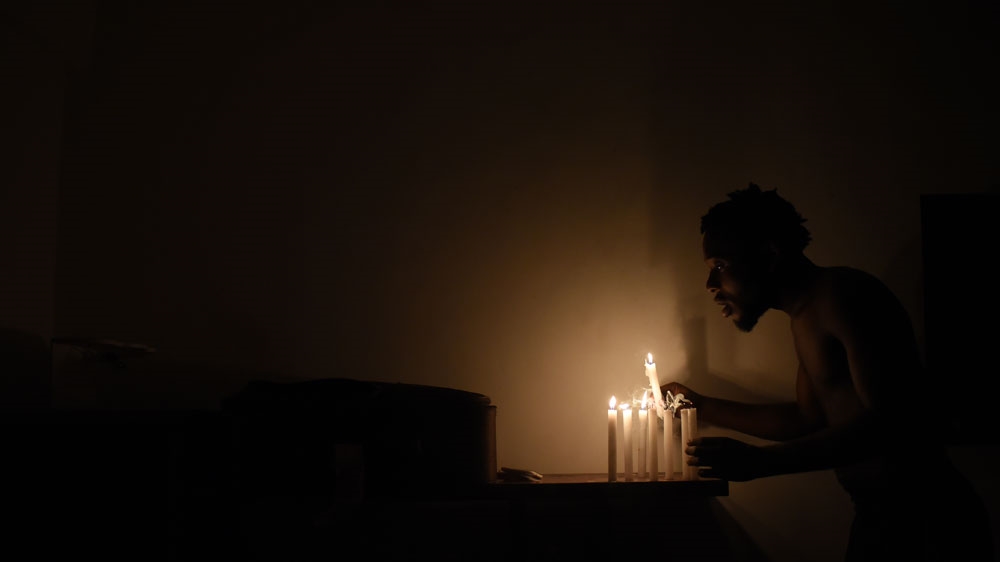 Chadrac Nkusu lights candles in his home. He has lived without electricity since the energy company cut the supply when he was unemployed [Fabio Teixeira/Al Jazeera] 