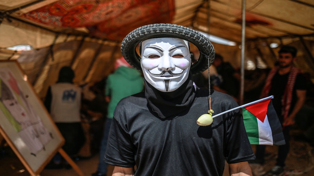 
A Palestinian protester wears a tyre on his head with an onion (to protect himself from tear gas) dangling from it [Hosam Salem/Al Jazeera]

