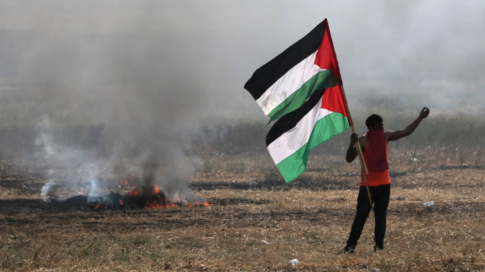 Protester holding Palestinian flags gestures during clashes with Israeli troops at Israel-Gaza border, in the southern Gaza Strip