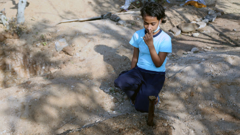 Rismawati's youngest daughter, Lydia, rests her hand on her mother's grave and says her final goodbye [Ted Regencia/Al Jazeera]