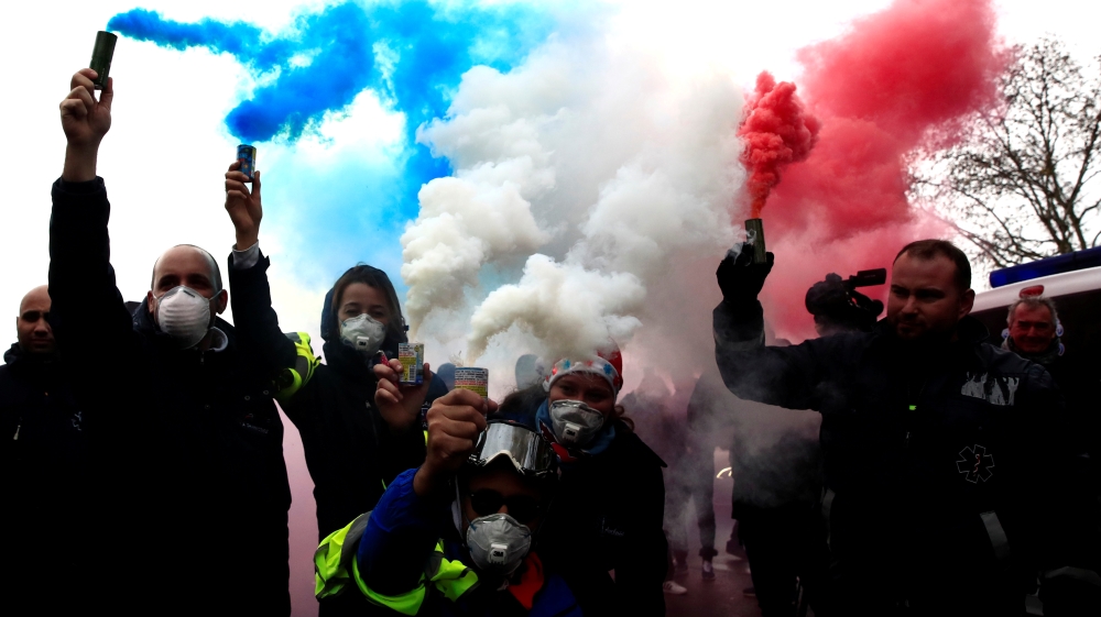 French ambulance drivers hold blue, white, red smoke bombs during a demonstration at the Place de la Concorde in Paris