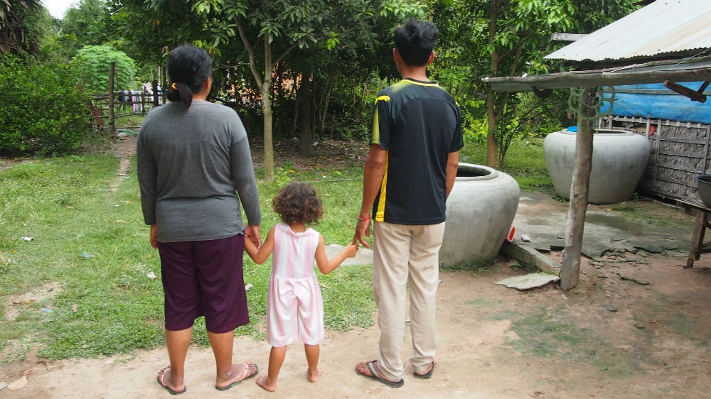 Poch Leng and Roen Ry at home with their granddaughter. Despite mounting loans, they are determined to care for their daughter's children, including her newborn son, who was conceived via IVF for adoptive parents in China. They did not want to show their faces on camera [Danielle Keeton-Olsen/Al Jazeera]