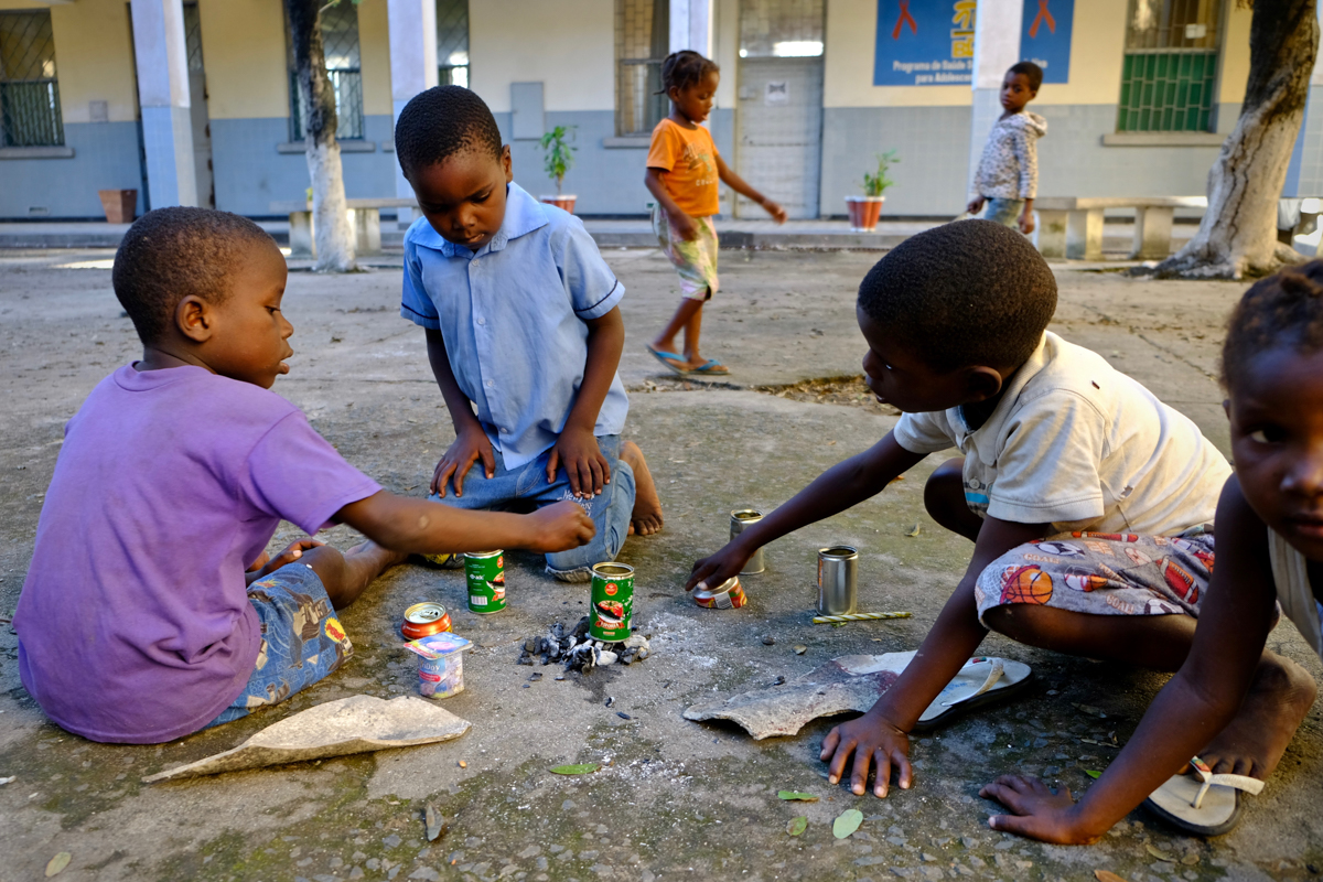 In the courtyard of this school, children boil tin cans of rain water on charcoal. Other children are drinking from puddles with spoons.