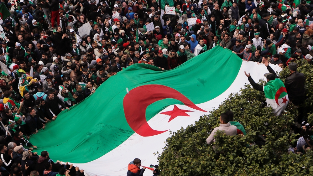 A demonstrator gestures from atop of a tree as others carry a giant national flag during a protest calling on President Abdelaziz Bouteflika to quit, in Algiers