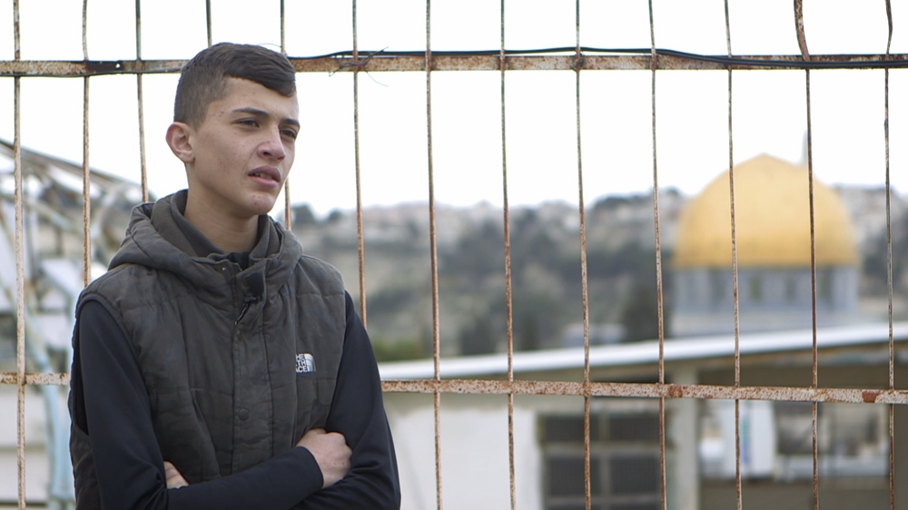 Mahdi Abu A'asab on the roof of his family home, nestled among Israeli settlers in Jerusalem, with the Al-Aqsa Mosque in the distance [Al Jazeera]